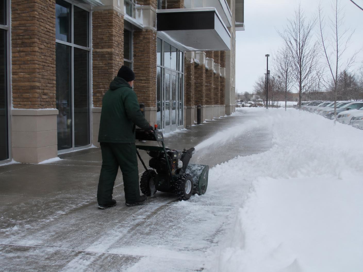 Crew member clearing a commercial sidewalk with a snow blower