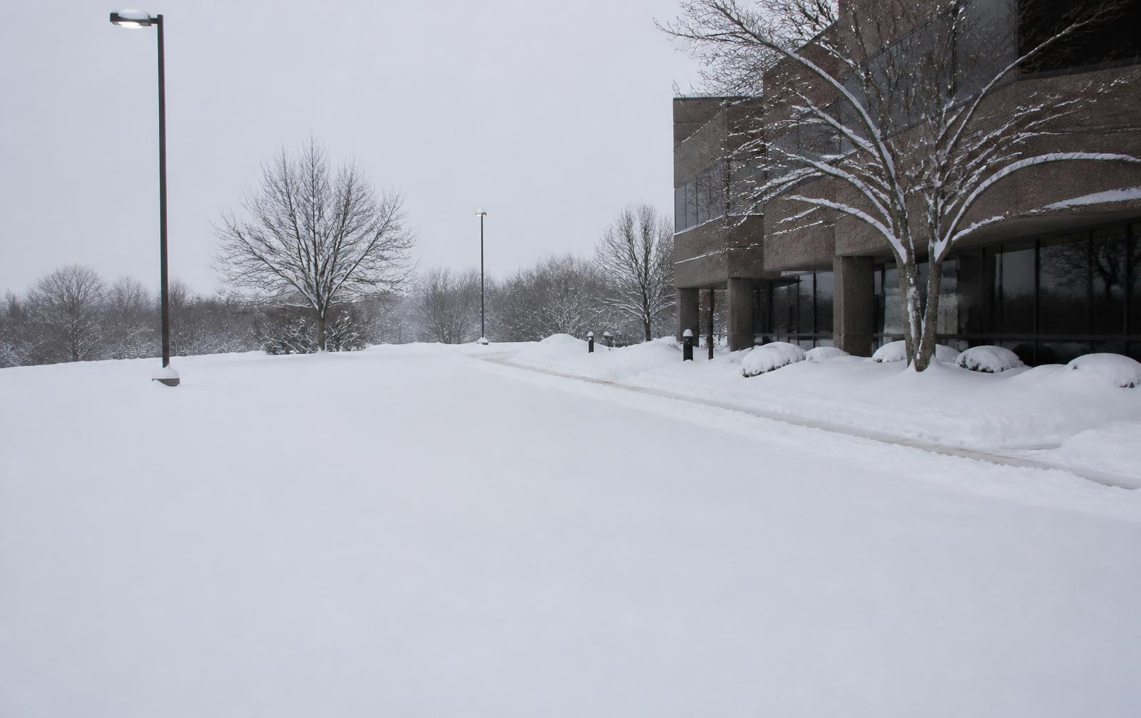 Commercial parking lot and sidewalk buried under snow before clearing
